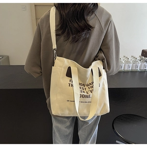 Detail of off-white canvas tote bag featuring adjustable strap and side pocket design