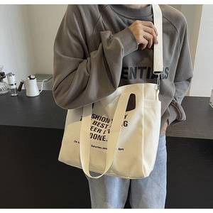 Off-white canvas tote bag worn on shoulder by model in a minimalist lifestyle setting