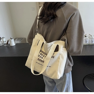 Detail of white canvas tote bag with black fashion lettering worn by a model