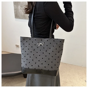 Detail of grey polka dot tote bag with black leather straps and silver bow pendant