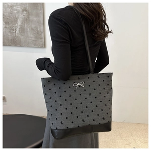 Detail of grey polka dot tote bag with bow embroidery and black leather base on shoulder