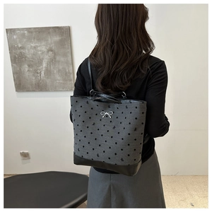 Detail view of gray polka dot canvas backpack with black leather base and bow embroidery