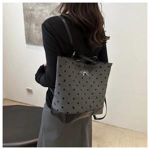Back view of gray polka dot backpack with metal bow clasp worn by a model in a minimalist room
