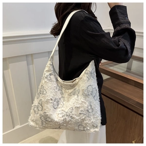 Detail of white canvas tote bag featuring grey butterfly embroidery and frayed tassel edges