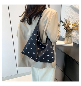 Detail of a black canvas tote bag featuring white bow patterns and a knotted shoulder strap