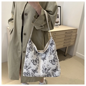 Detail of white tote bag with black butterfly print and fringe edges on a model