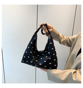 Detail of black hobo bag with white bow pattern held by hand against a minimal background
