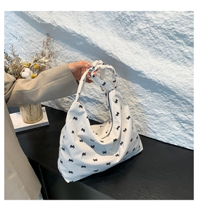Close-up of white canvas tote bag with black bow print and knotted shoulder strap