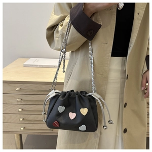 Detail of black drawstring bucket bag with colorful leather heart patches and chain strap