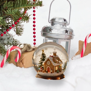 Nahaufnahme einer leuchtenden Weihnachtskristallkugel mit Lebkuchenhaus und warmen LEDs