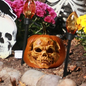 Detailed view of Halloween pumpkin sculpture with skull face design in a garden setting