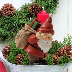 Nain de jardin de Noël avec sac de cadeaux dans un décor festif de branches de pin