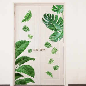 Detail of green tropical palm and monstera leaf wall stickers on a white door