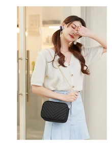 Detail of black V-quilted camera bag with golden chain strap on model for urban style
