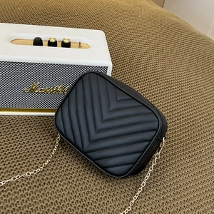 Chic black V-quilted camera bag with gold chain strap on textured brown fabric