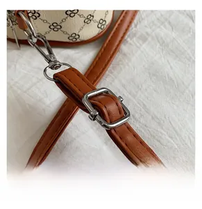 Detail of adjustable brown leather shoulder strap with silver metal buckle on printed handbag