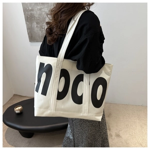 Detail view of a white large-capacity tote bag with black npco print on model shoulder