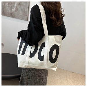 Detailed view of a white tote bag with large black hoco letters carried by a model
