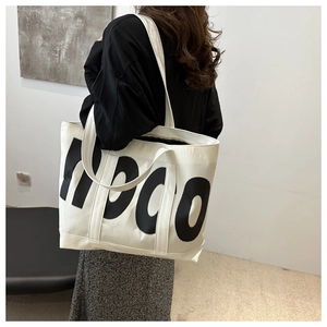 Detail shot of the large beige canvas tote bag with black HDO letters worn by a model