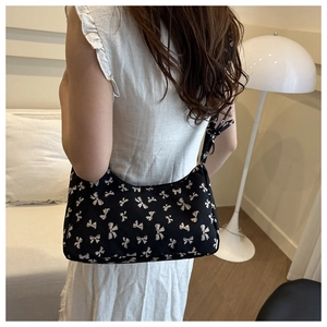 Detail of black underarm bag with white bow pattern worn by model in minimalist interior