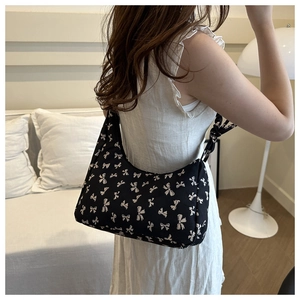 Detail of black hobo shoulder bag with white bow pattern and side ribbon ties