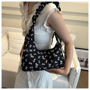 Detail view of black pleated shoulder bag with white bow print and ribbon decoration