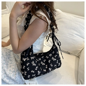 Detail of black shoulder bag with white bow pattern and ruffled handle in lifestyle setting