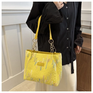 Detalle del bolso tote de lona amarilla con relieve, bordado ondulado y cadena