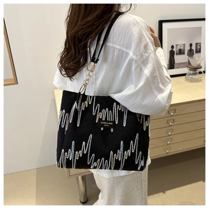 Detalle del bolso tote negro con bordado arcoíris y cadena dorada llevado por una modelo