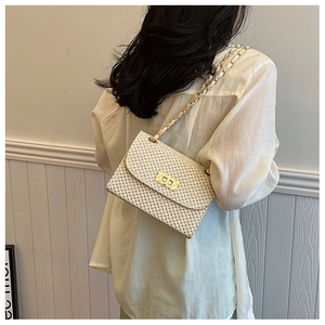 Detail of cream woven texture and golden chain strap on a small crossbody square bag