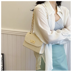 Detail of beige woven straw shoulder bag featuring a gold chain strap and metal lock