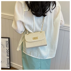 Detail of a beige woven straw crossbody bag featuring a gold lock and chain strap on a model