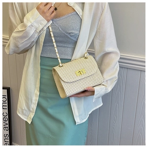 Detailed view of woven straw crossbody bag featuring golden twist lock and chain strap