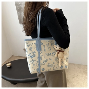 Dettaglio di una grande borsa tote in PU bianca con stampe graffiti blu e ciondolo a orso
