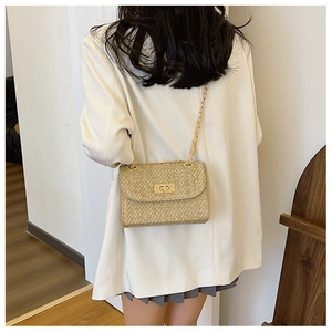 Detail of golden straw crossbody bag with metal chain strap and turn-lock on a model