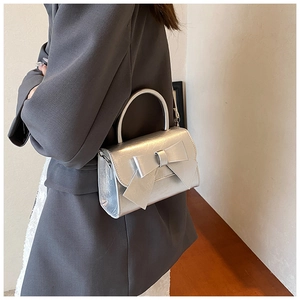 Silver bow shoulder bag shown with grey blazer and white dress for a stylish look