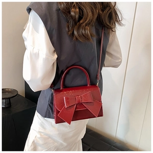 Close-up of a red patent leather handbag with a large bow and elegant handle