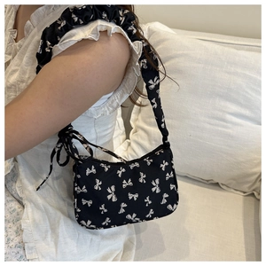 Detail of black shoulder bag with white bow prints and ruched strap on a white sofa