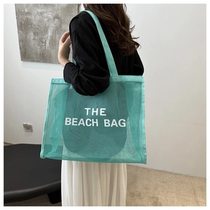 Detail shot of a mint green mesh beach tote bag with THE BEACH BAG text on a model