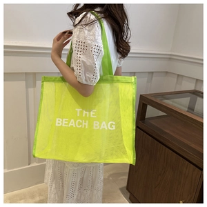Detail of neon green mesh tote bag featuring bold THE BEACH BAG white lettering