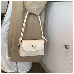 Detail of a creamy white underarm bag with a metallic bow buckle and knotted shoulder strap