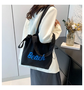 Detailed shot of black canvas tote bag featuring blue artistic Beach lettering design