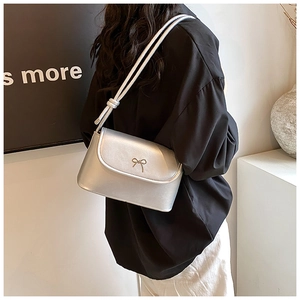 Detailed back view of a silver shoulder bag with metallic bow and dual round straps on model