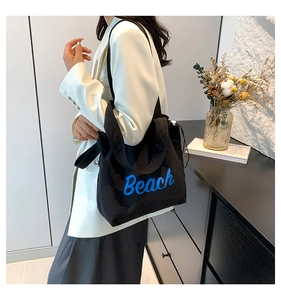 Close-up of black canvas tote bag featuring blue Beach lettering worn by a model