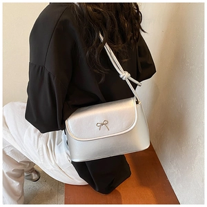 Detail of silver shoulder bag showing elegant metal bow buckle and knotted strap texture