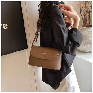 Close-up of a brown leather shoulder bag featuring a gold metal bow on the front flap