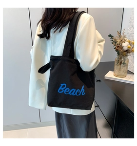 Detail of a black canvas tote bag featuring a blue cursive Beach print on a shoulder strap