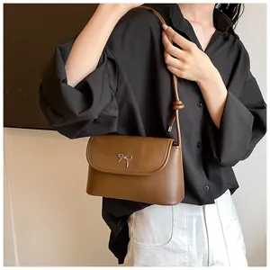 Detail of a brown PU leather shoulder bag featuring a golden metal bow and knotted strap