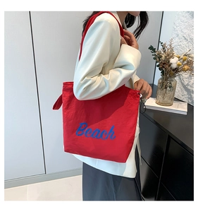 Detailed view of the vibrant red canvas tote bag with blue Beach script and drawstring detail