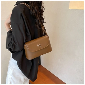 Side view of a brown leather crossbody bag with a golden bow detail on a model